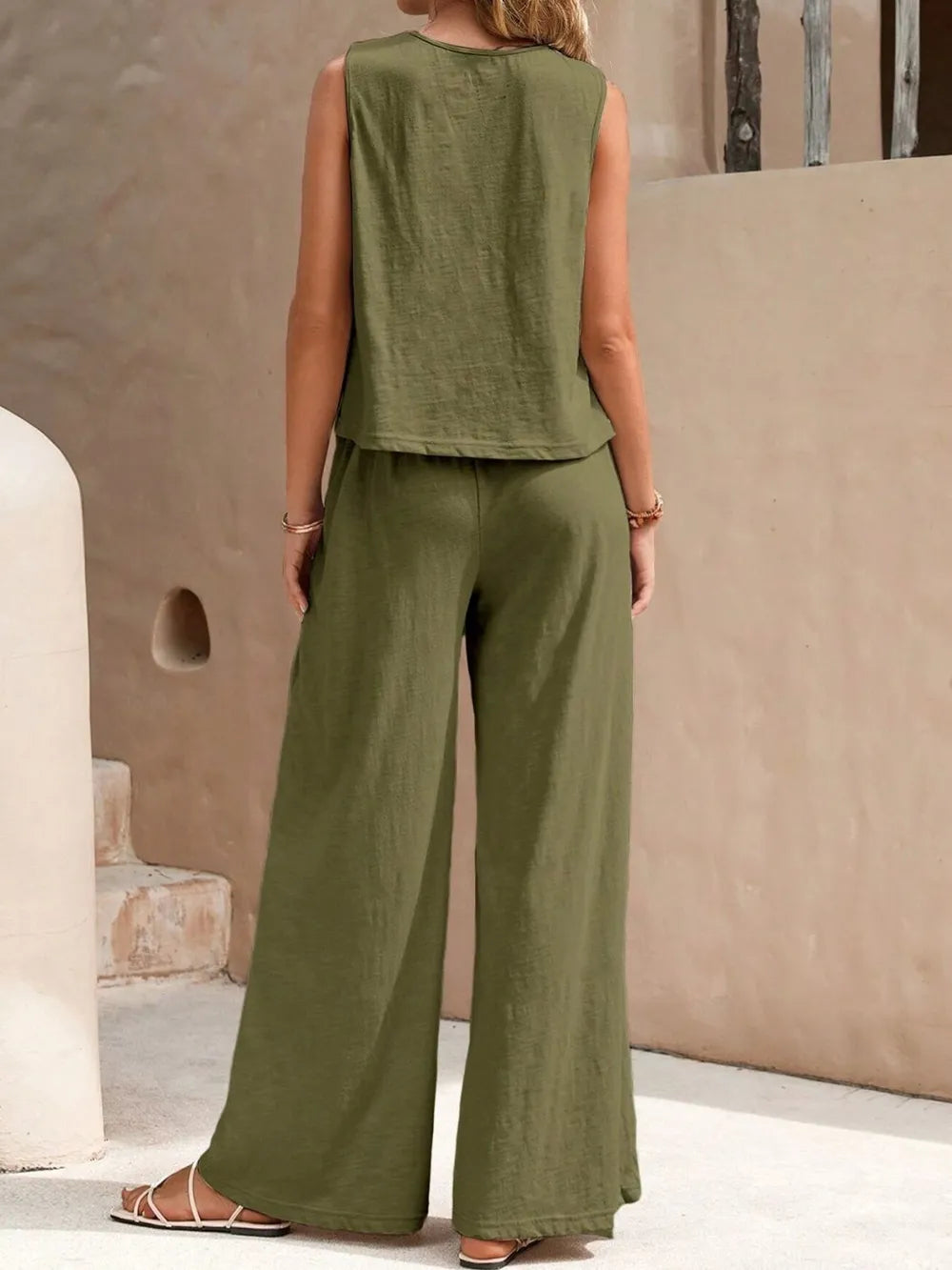 Person wearing an olive green sleeveless top and wide-leg pants in a neutral setting.