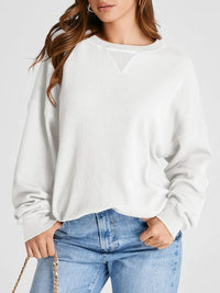 Woman wearing a white sweater and blue jeans on a plain background
