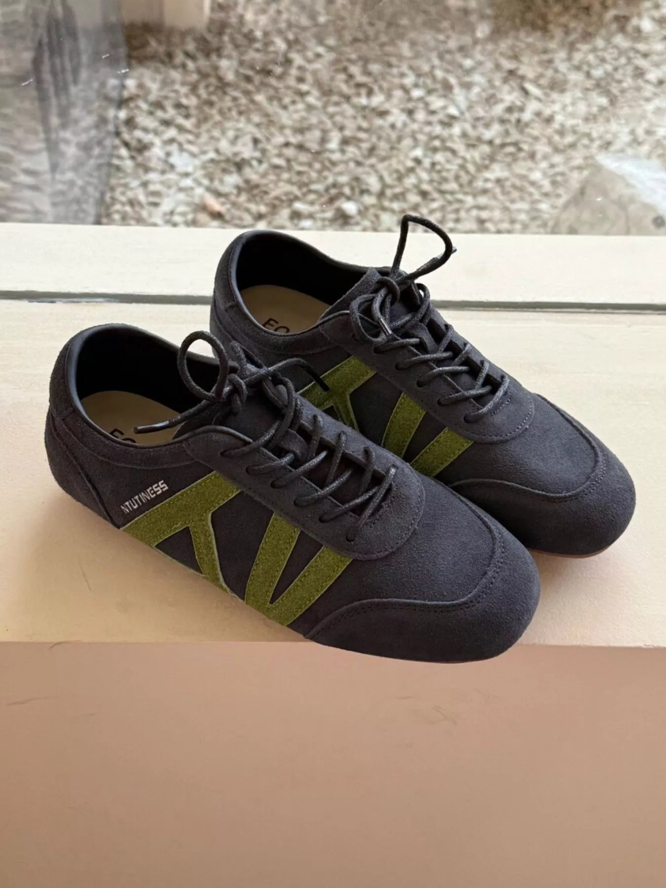 Pair of black sneakers with green accents on a reflective surface