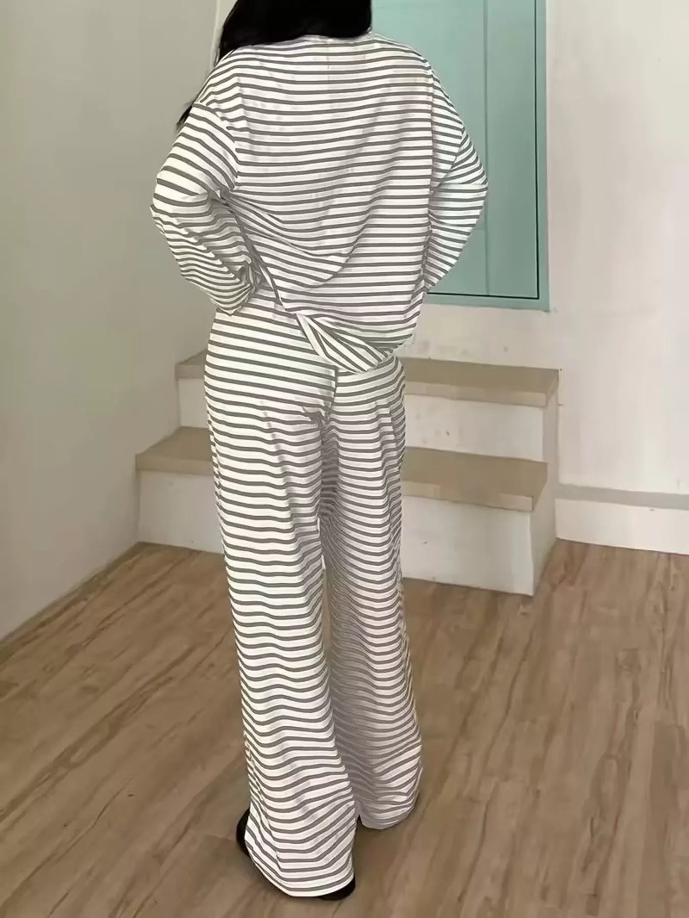 Person wearing a black and white striped outfit in a room with wooden floor and light green wall.
