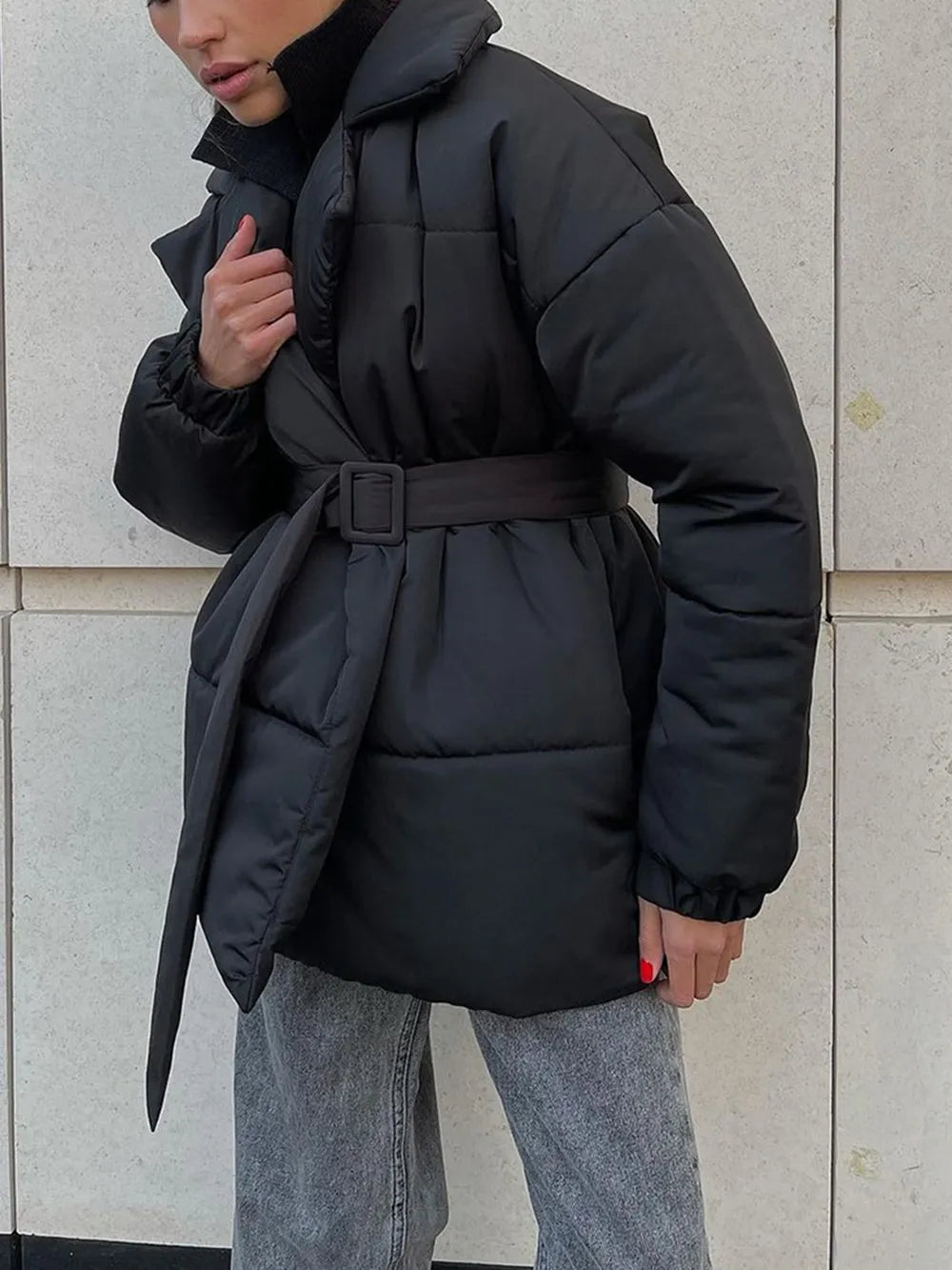 Person wearing a black puffer coat against a light gray wall.