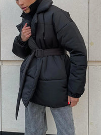 Person wearing a black puffer coat against a light gray wall.