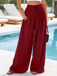 Person wearing burgundy wide-leg pants by a poolside.