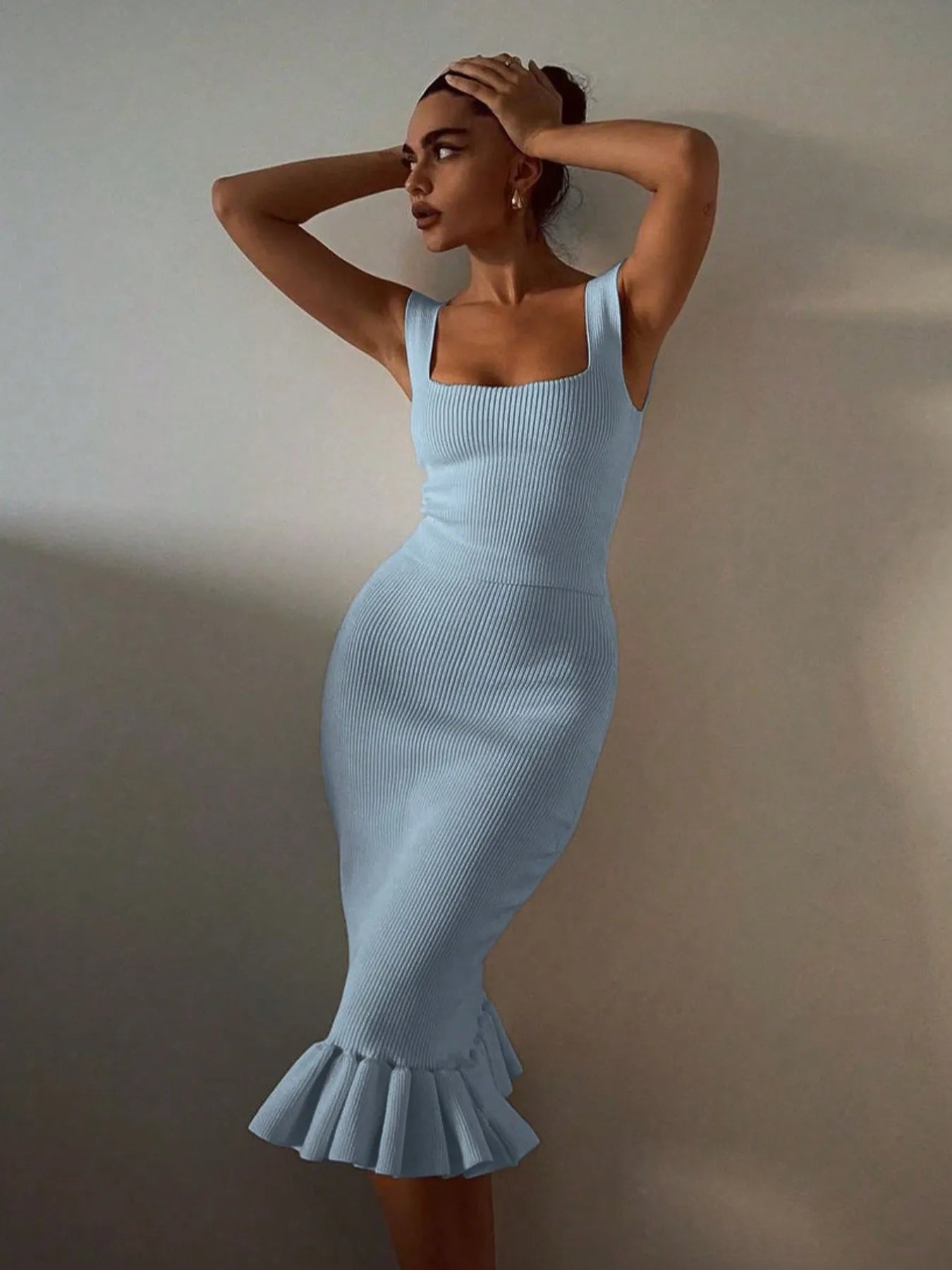 Woman wearing a light blue dress with a ruffled hem against a plain background