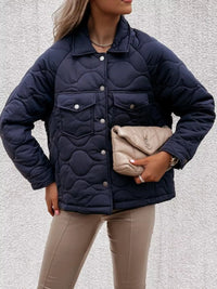 Person wearing a navy quilted jacket holding a beige handbag against a neutral background