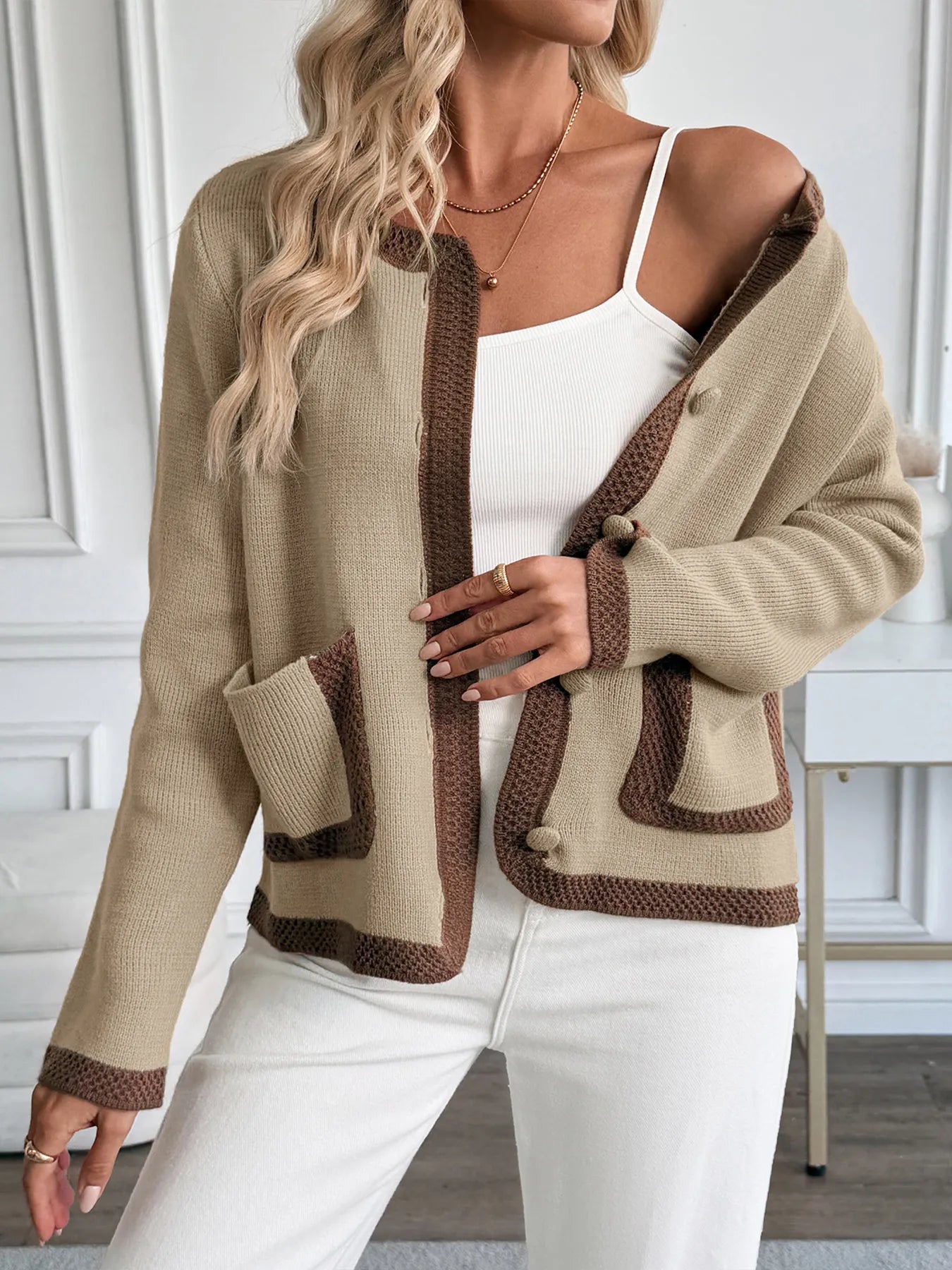 Woman wearing a beige cardigan with brown accents indoors.