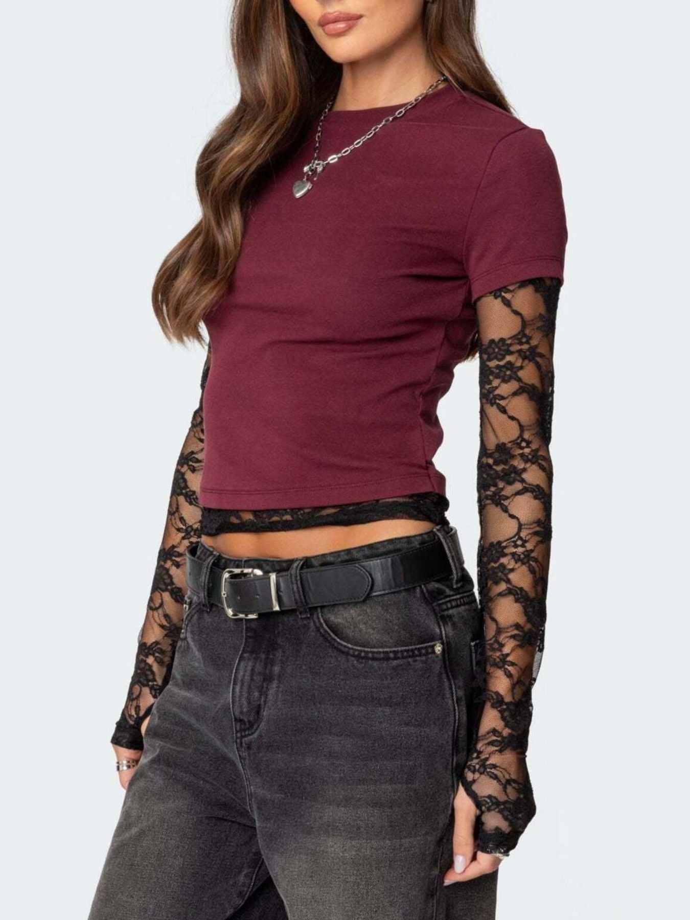 Woman wearing a burgundy top with lace sleeves and black jeans on a white background