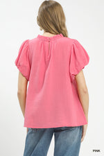 Woman wearing a pink textured top with ruffled sleeves on a white background