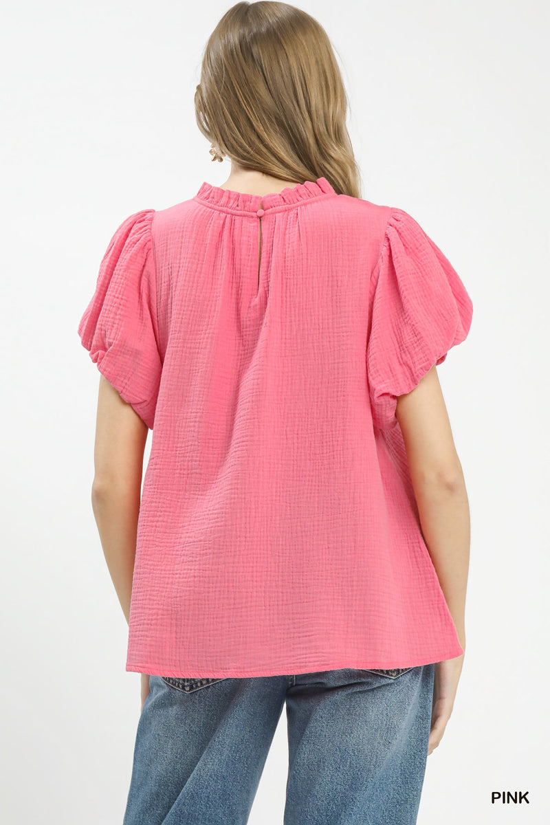 Woman wearing a pink textured top with ruffled sleeves on a white background