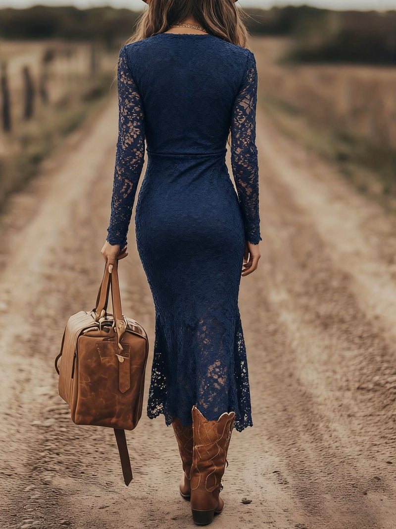 Woman in a blue lace dress and brown boots walking on a dirt road with a leather bag.