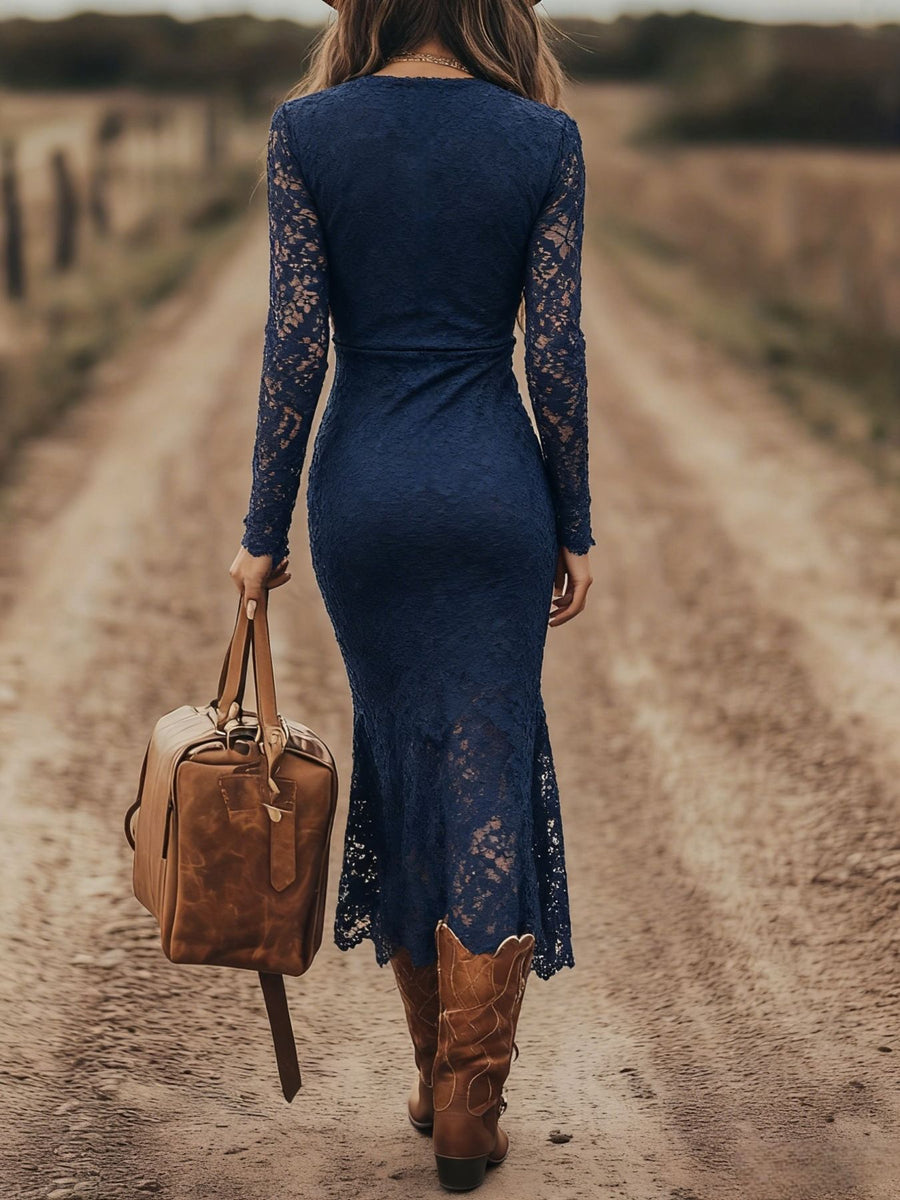 Woman in a blue lace dress and brown boots walking on a dirt road with a leather bag.