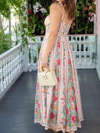 Woman in a floral dress holding a cream handbag on a porch with plants in the background