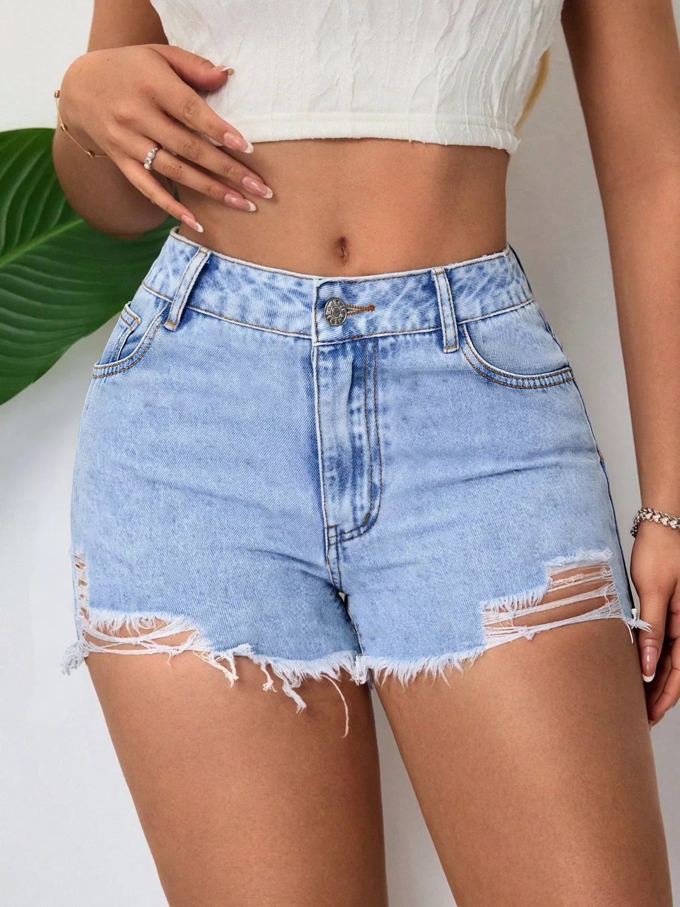 Person wearing light blue denim shorts with a white top against a neutral background