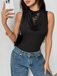 Woman wearing a black sleeveless top with mesh details and blue jeans, taking a selfie.