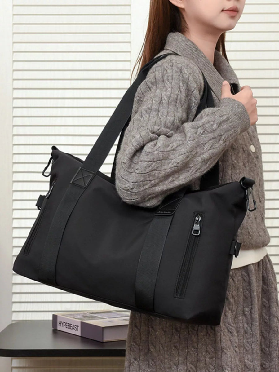 Person holding a black shoulder bag with a neutral background