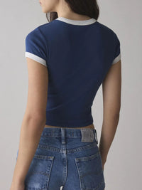 Person wearing a blue crop top with white trim and blue jeans on a gray background