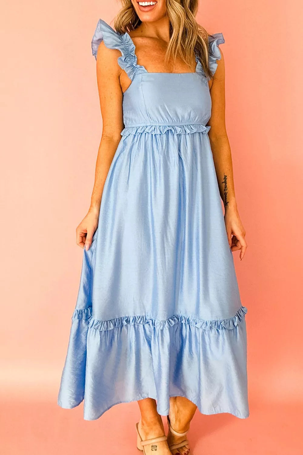 Woman wearing a light blue dress with ruffled sleeves against a pink background
