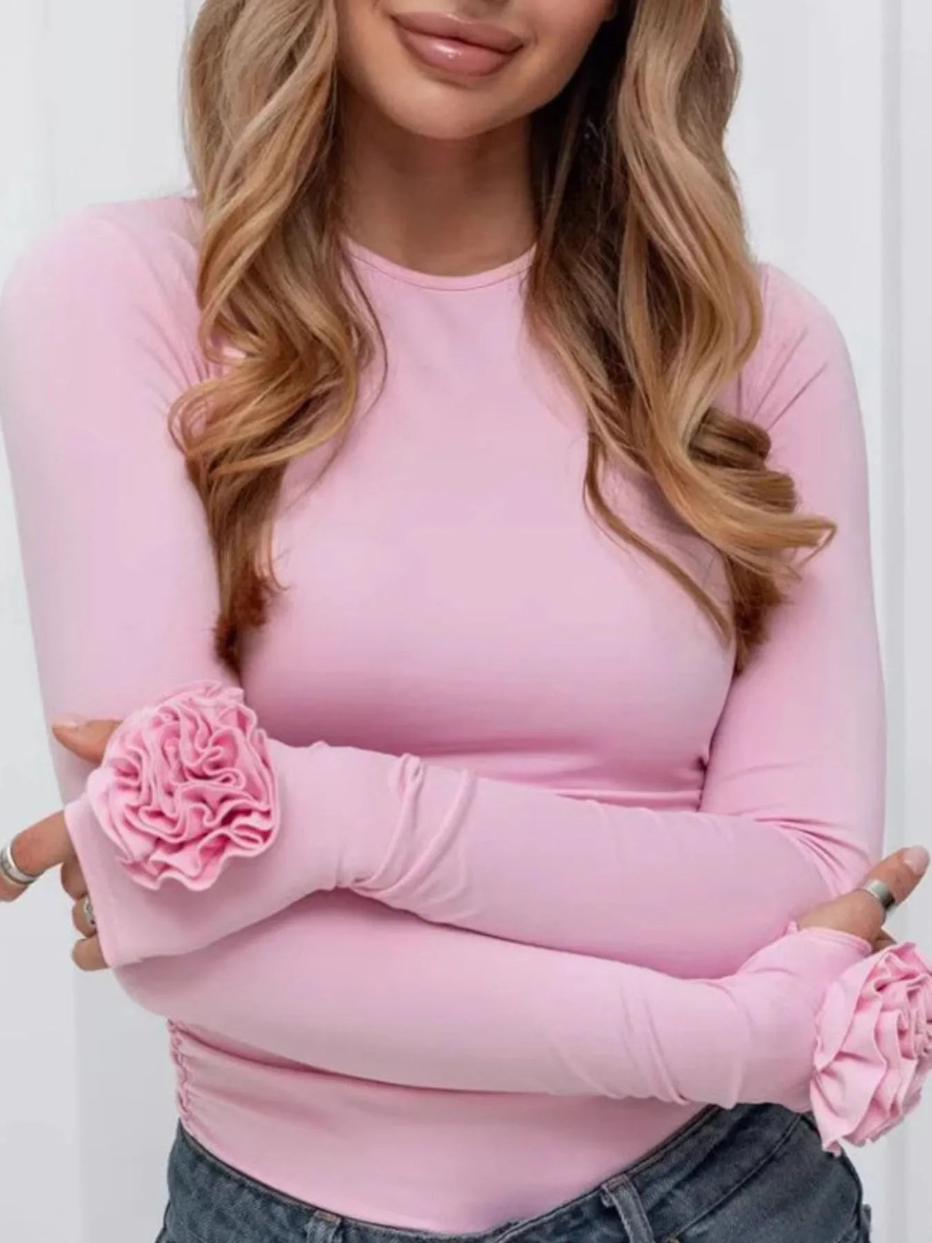 Woman wearing a pink long-sleeve top with floral elbow patches against a white background