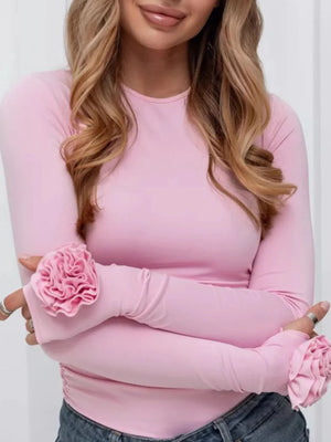 Woman wearing a pink long-sleeve top with floral elbow patches against a white background