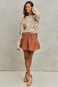 Woman wearing a floral sweater and brown skirt against a plain background