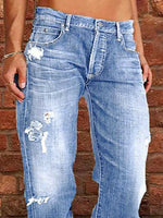 Blue jeans with floral designs worn by a person against a brick wall.