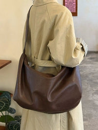 Person wearing a beige jacket with a brown leather bag indoors.