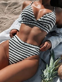 Person wearing a black and white striped bikini on a sandy beach with a pineapple and coconut in the foreground.