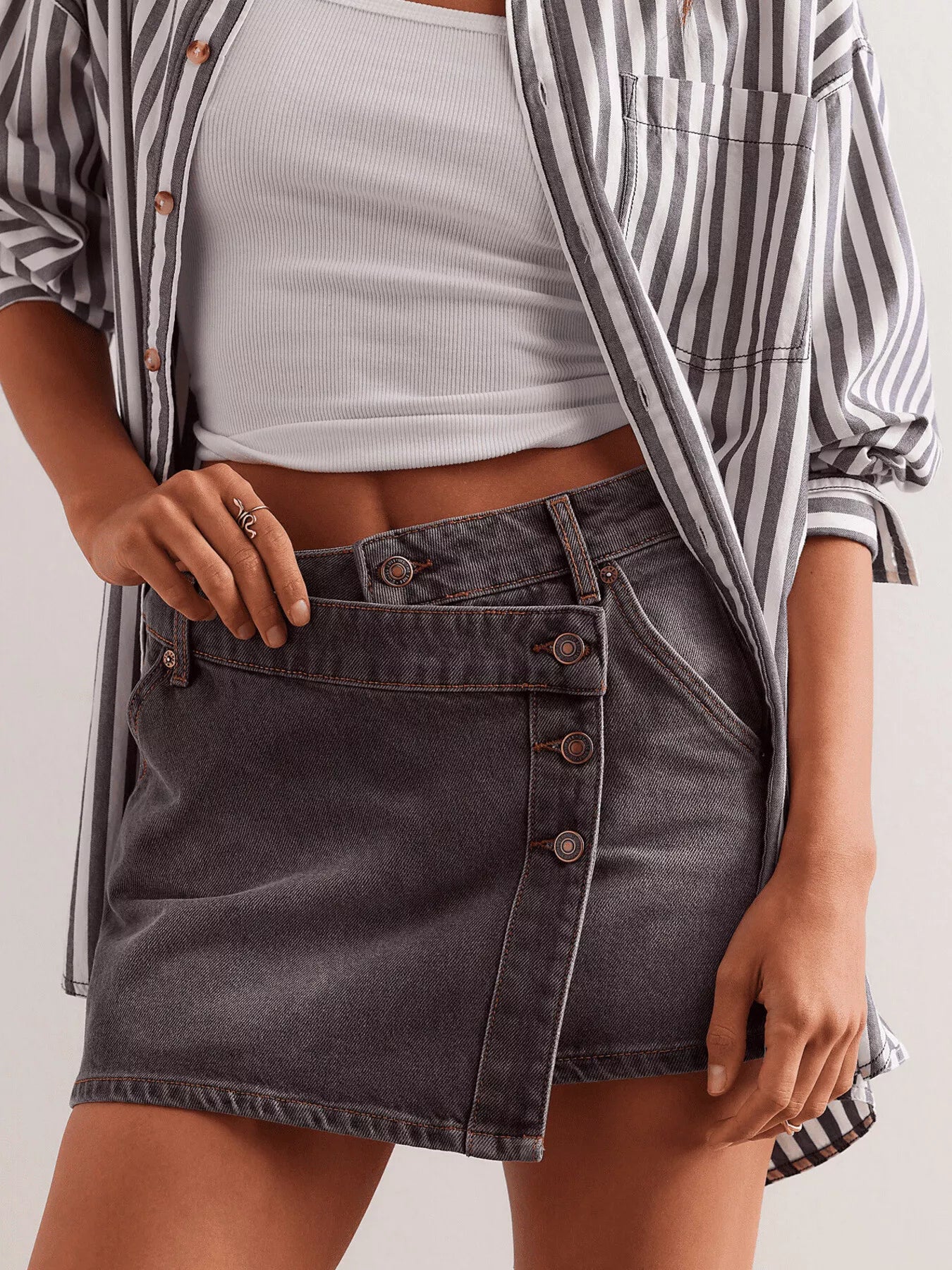 Person wearing a striped shirt over a white top and black denim skirt on a light background