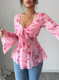 Woman wearing a pink floral blouse with a bow detail and blue jeans against a neutral background