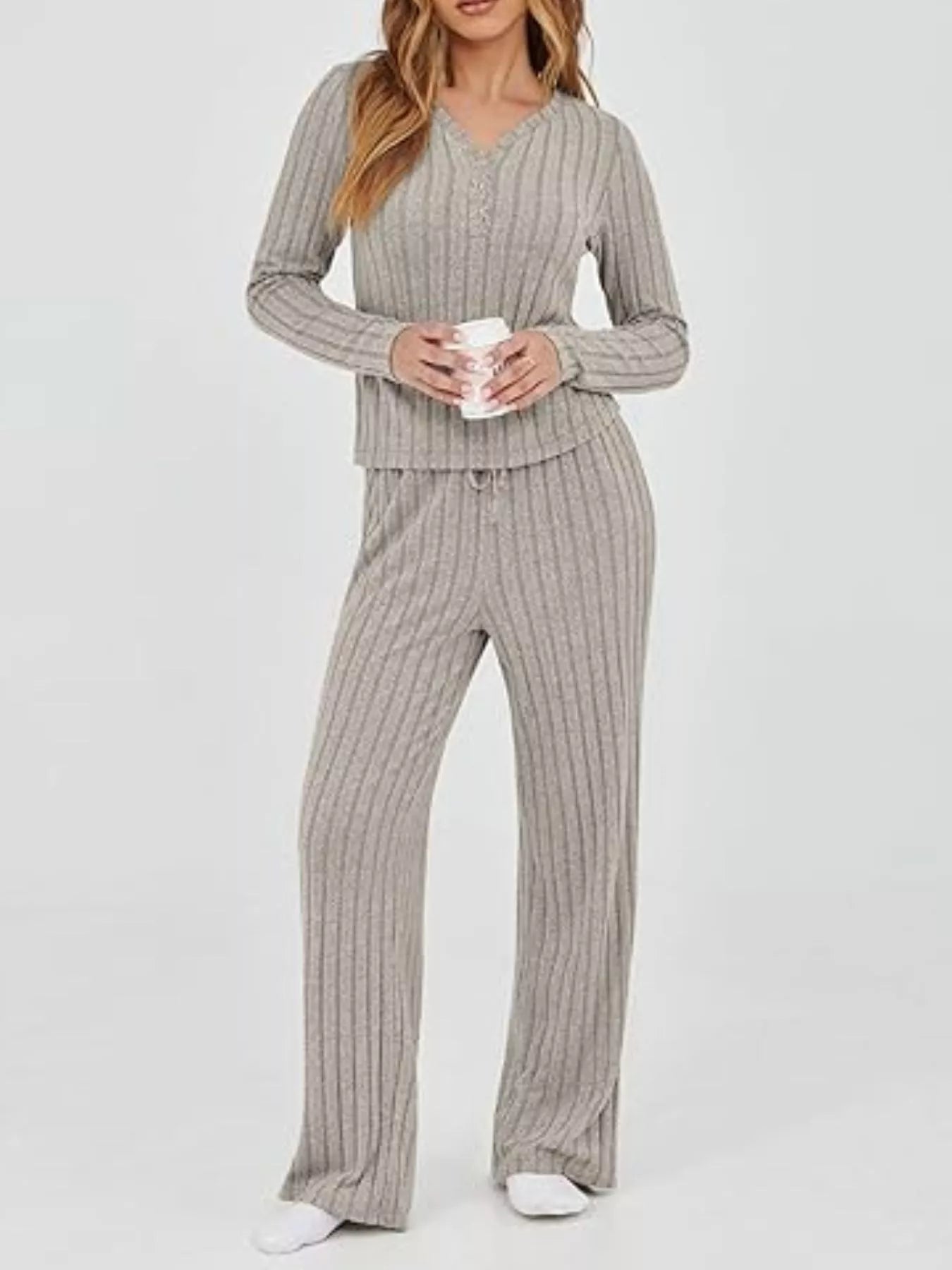 Woman wearing a gray ribbed pajama set holding a mug on a white background