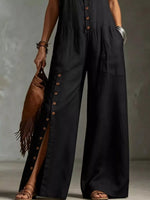 Person wearing a black jumpsuit with button details, holding a brown leather bag against a neutral background.