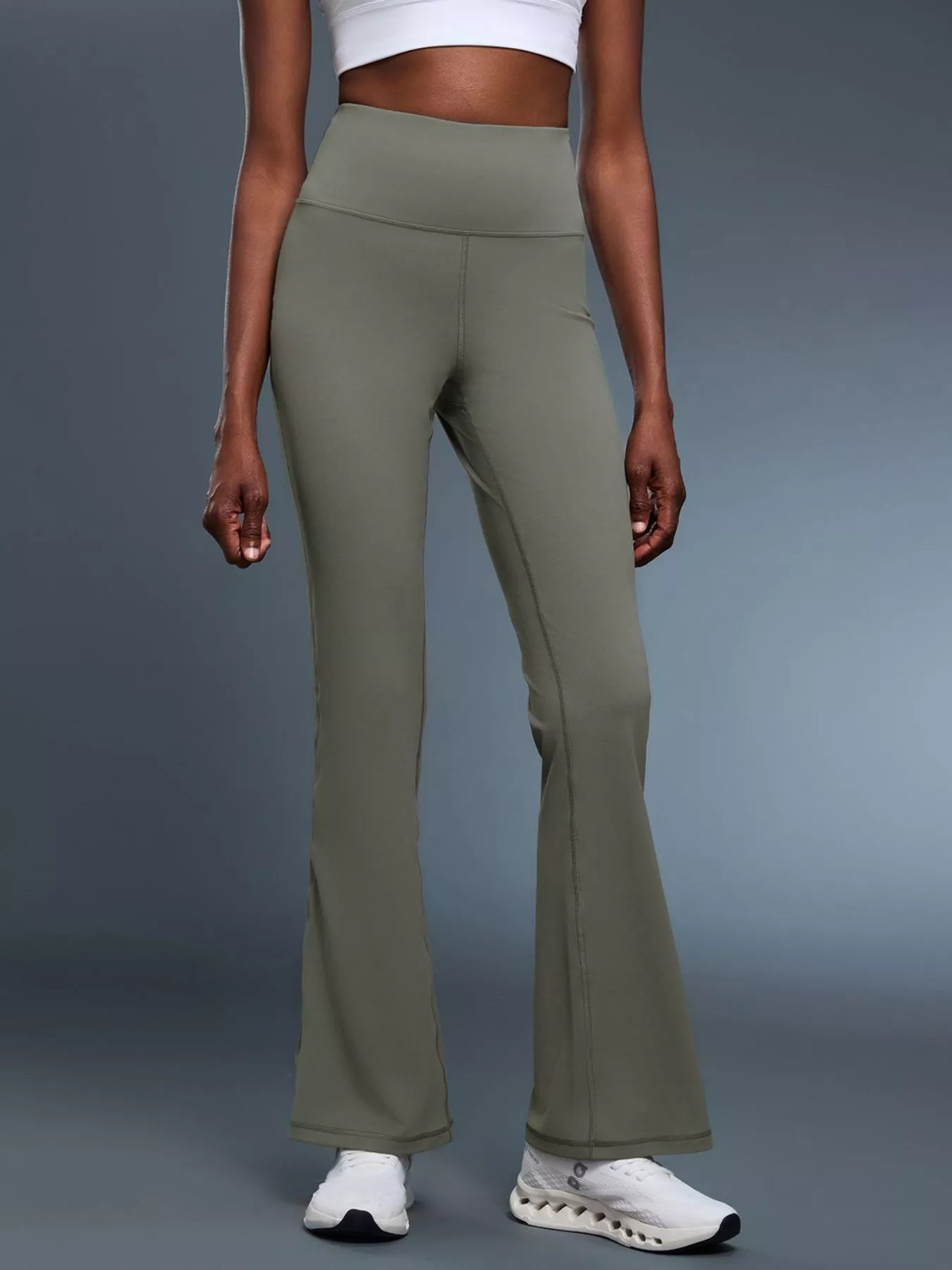 Person wearing olive green flared pants on a gray background
