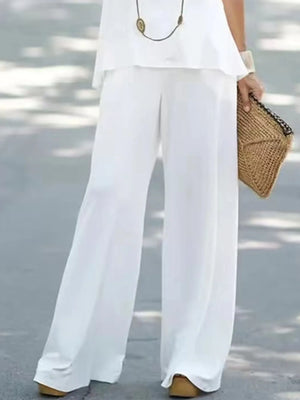 Person wearing white wide-leg pants and holding a woven bag on a blurred outdoor background