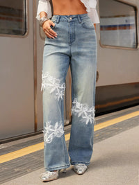 Person wearing light blue jeans with floral embroidery on a train platform.
