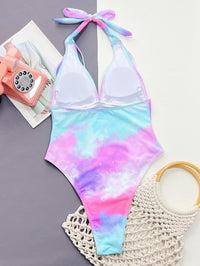 Multicolored tie-dye swimsuit with a pink phone and beige bag on a gray surface