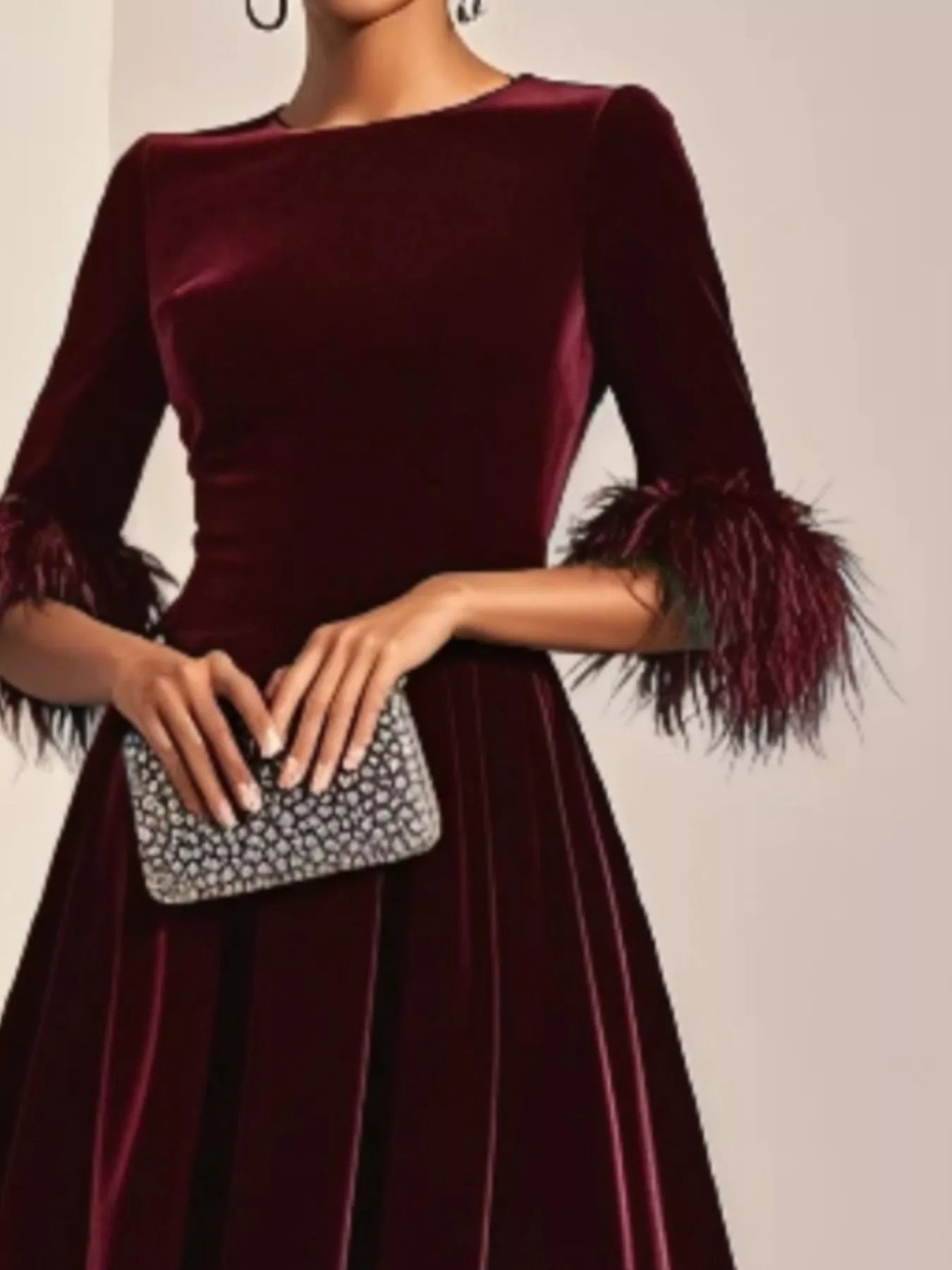 Burgundy velvet dress with feathered cuffs held by a hand with a silver clutch.