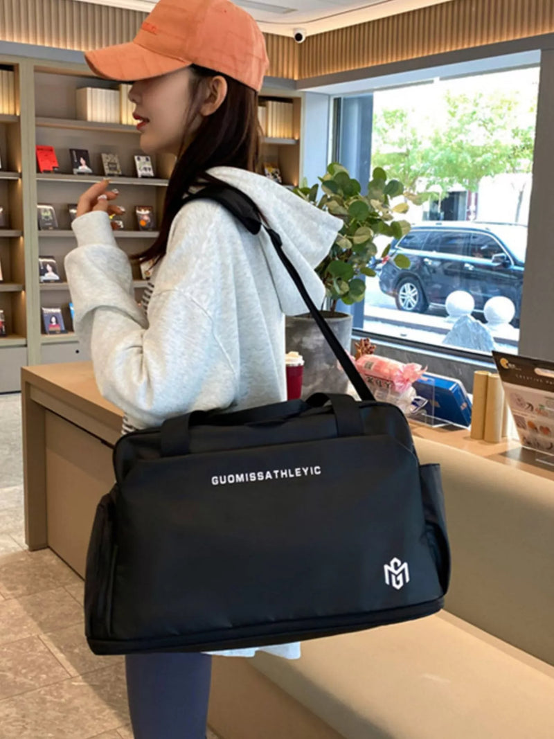 Person holding a black duffel bag with a brand logo in an indoor setting.