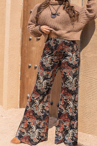 Person wearing a brown sweater and patterned pants against a beige wall.