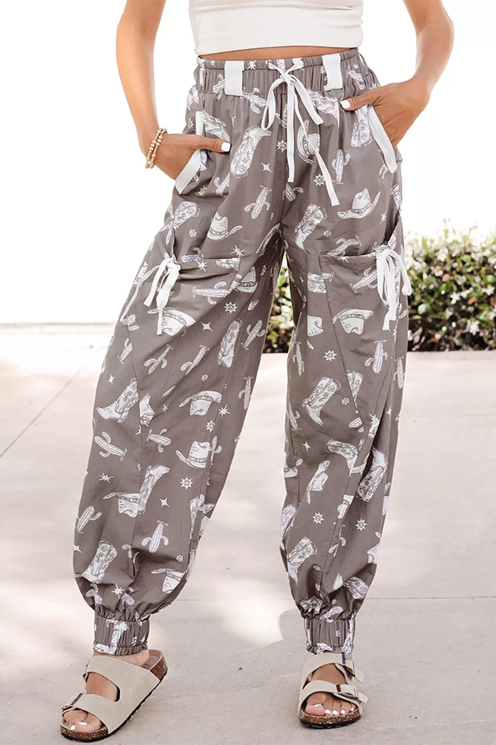 Person wearing gray patterned pants with a white top and sandals on a light background