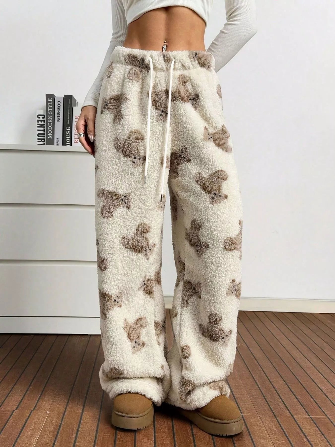 Person wearing white fleece pants with bear pattern and brown boots indoors.