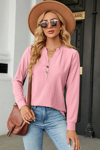 Woman wearing a pink long-sleeve top, blue jeans, and a brown hat with sunglasses outdoors.