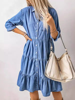 Woman wearing a blue denim dress holding a beige handbag against a light background