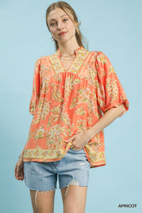 Woman wearing a floral apricot blouse and denim shorts on a light blue background