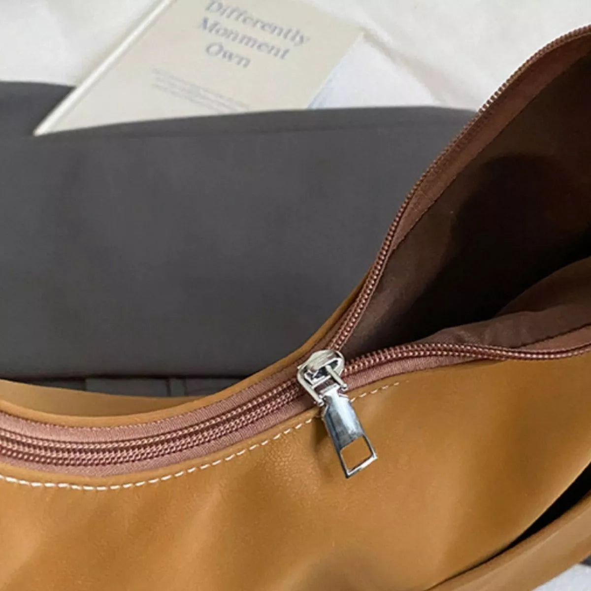 Close-up of a brown leather bag with a zipper, partially open, on a light background.
