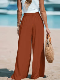 Person wearing rust-colored wide-leg pants on a beach.