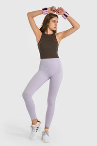 Woman wearing a brown tank top and light purple leggings on a white background