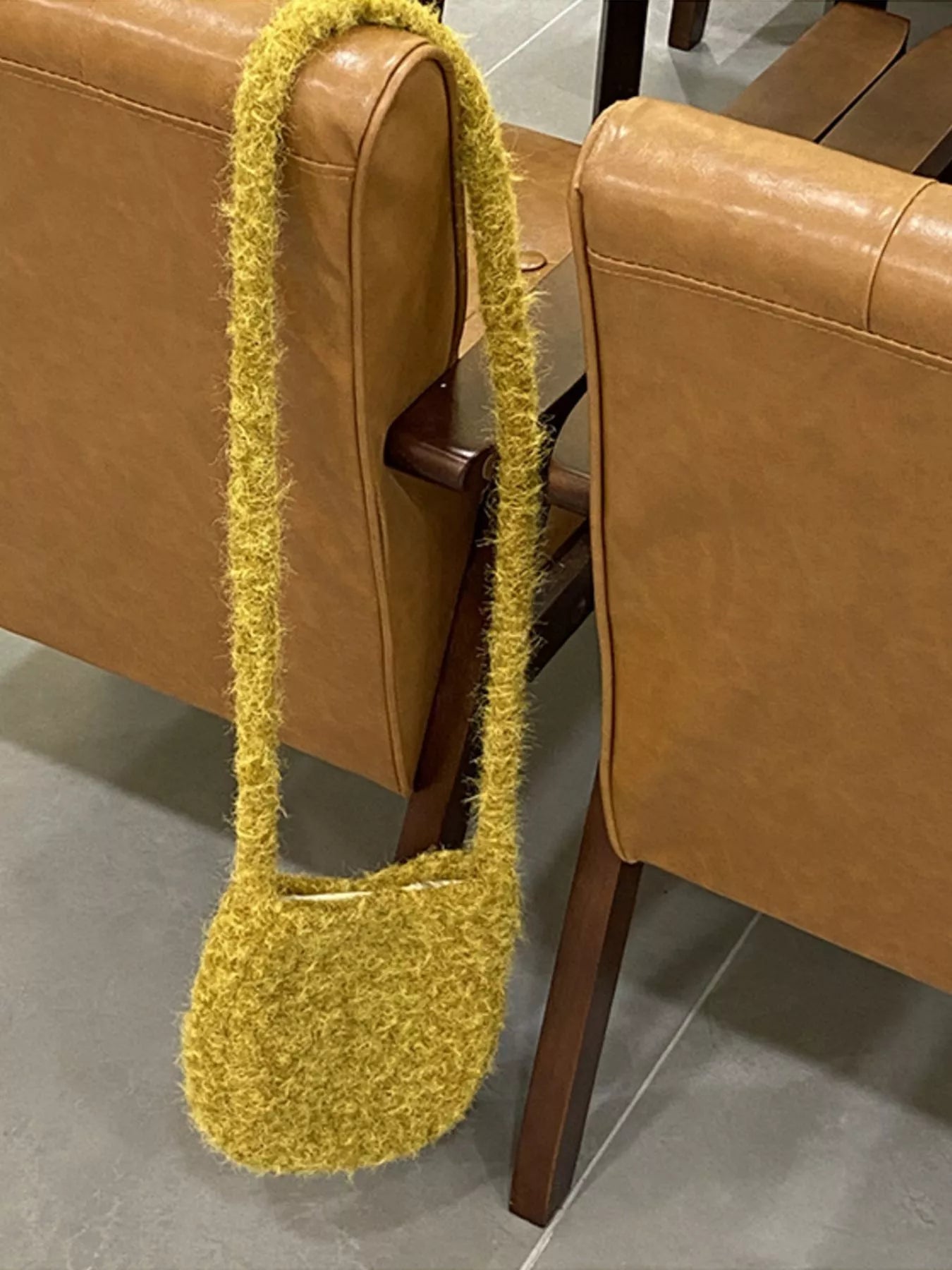 Yellow textured handbag hanging on a brown leather chair.