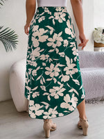 Person wearing a green floral skirt in a room with a couch and plant.