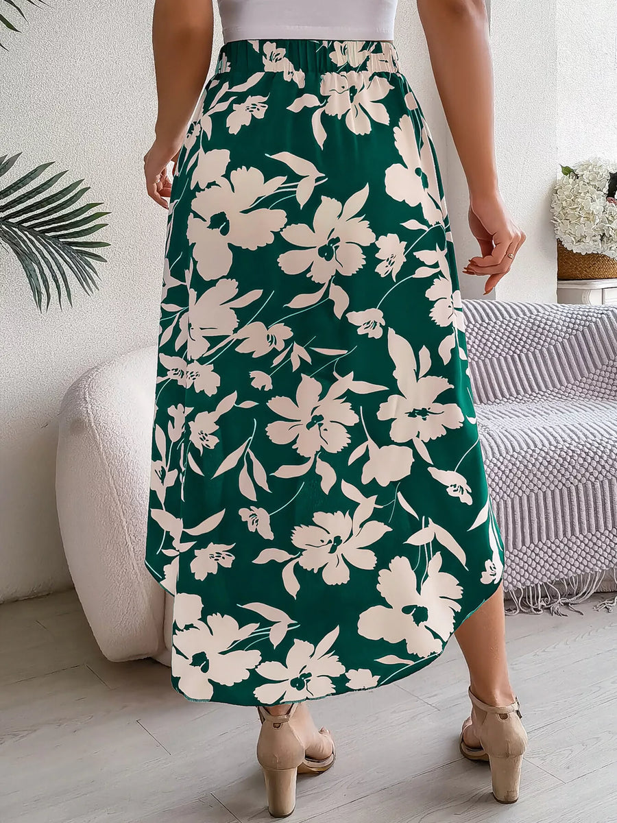 Person wearing a green floral skirt in a room with a couch and plant.