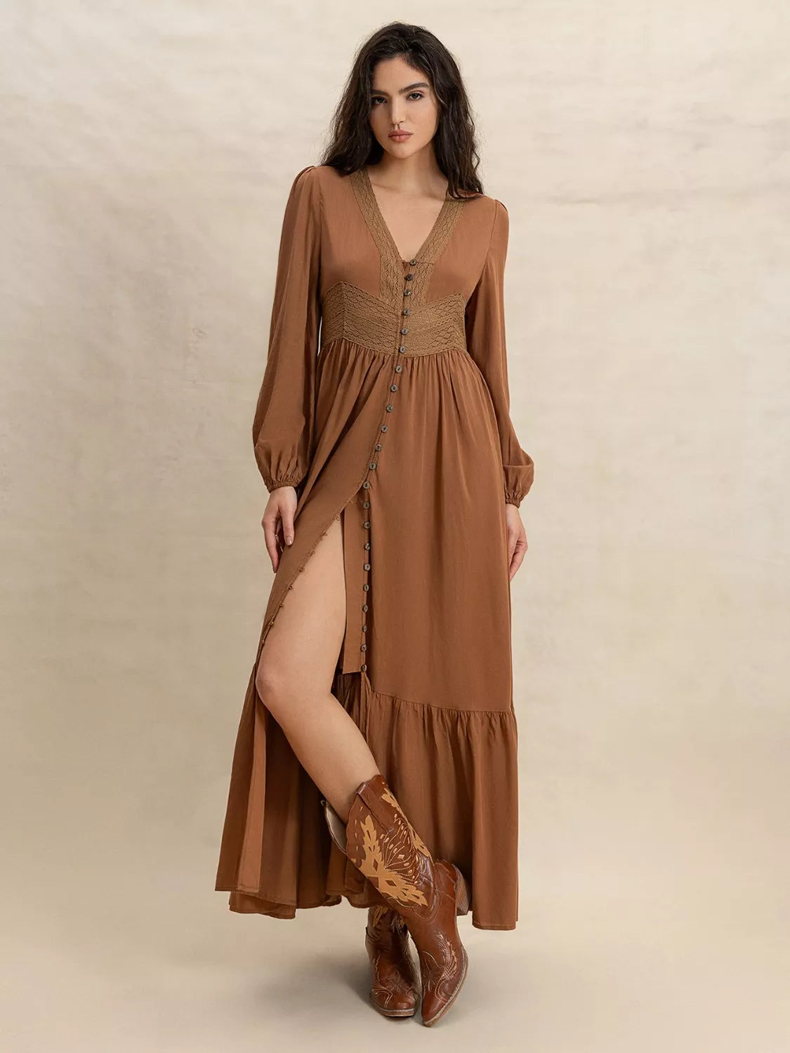 Woman wearing a long brown dress with a slit and matching boots on a beige background